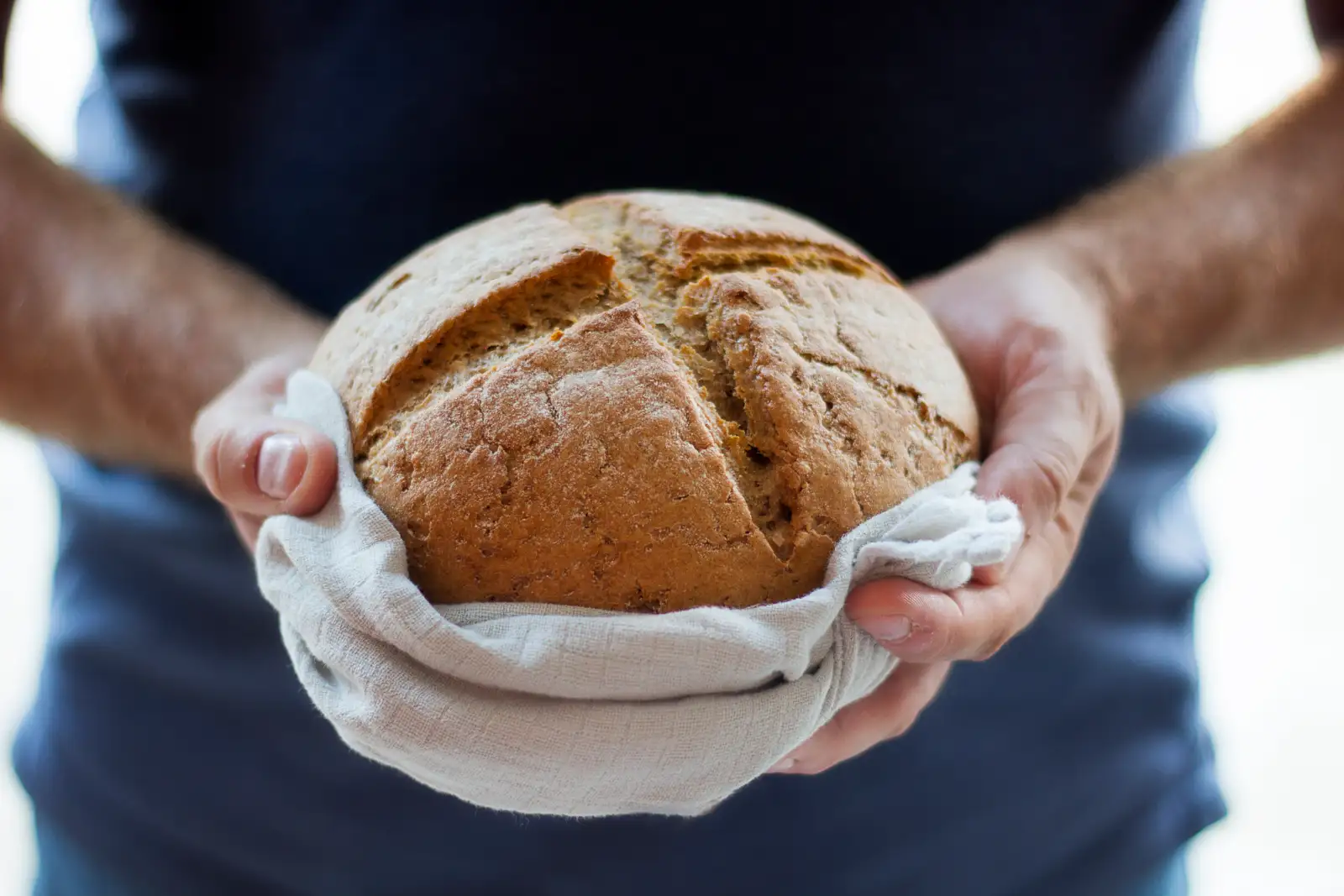 Hands holding a round crusty loaf wrapped in a white cloth