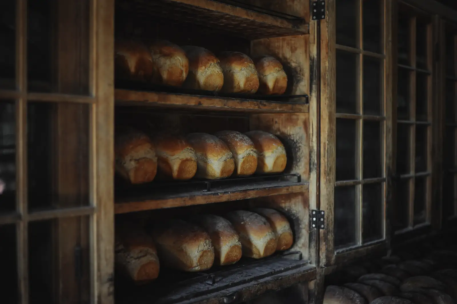 Rows of golden crusty loaves on the shelves of a wooden bakery rack